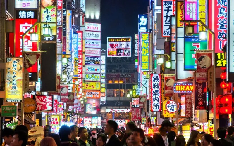 Busy neon-lit street in Osaka at night with a large crowd.